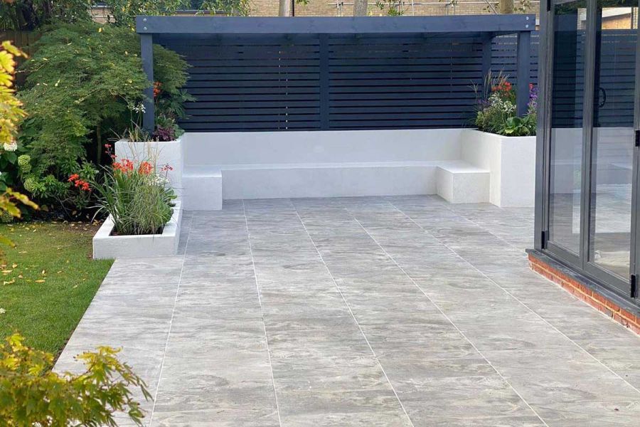 Marble Grey porcelain paving patio between lawn and doors of house, with pergola- covered seating area. Design by Elitescapes.