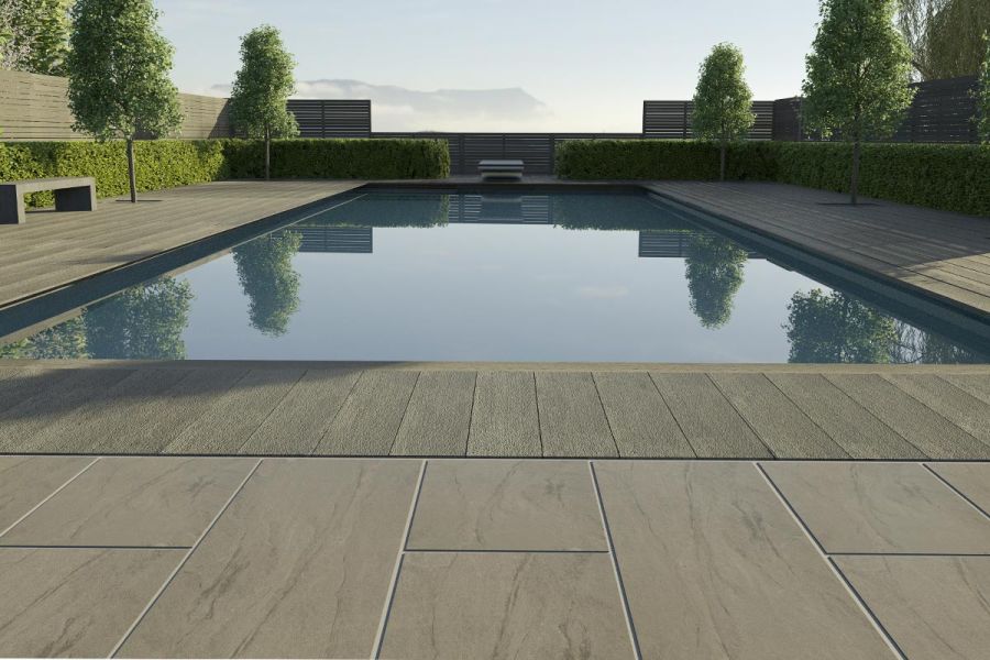 Swimming pool terrace edged with low hedges. Paved surround of Marble Grey outdoor vitrified tiles and composite decking.