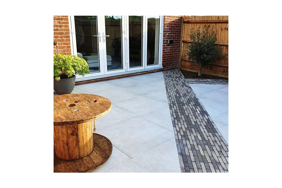 Diagonal stripe of Silver Multi Clay pavers runs to corner of house past giant bobbin table on grey paving by Marli Construction.