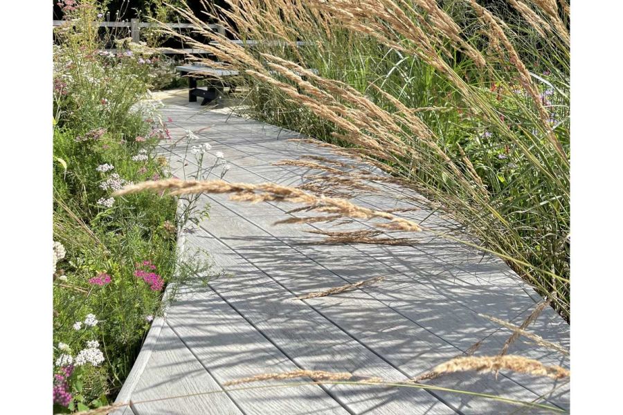 Tall grasses bend over sinuous path of Millboard Smoked Oak grey composite decking. Built by Shaun’s Gardening and Landscaping.