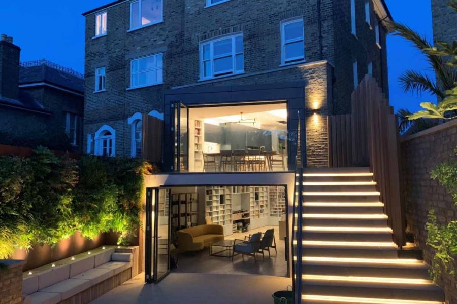 Rear of tall period house with lit-up basement steps rising to kitchen above from area paved with Britannia Buff sawn York stone.