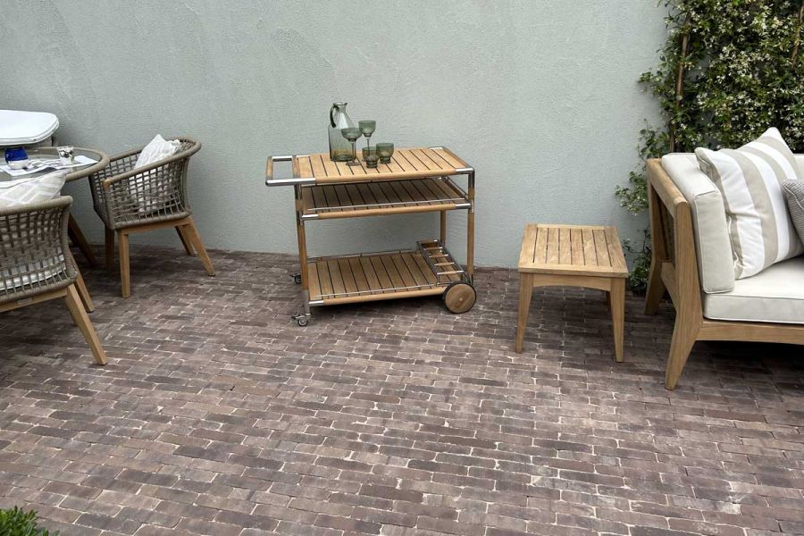 Wood and metal hostess trolley and low table sit against painted wall on Verona brick paving between dining set and sofa.