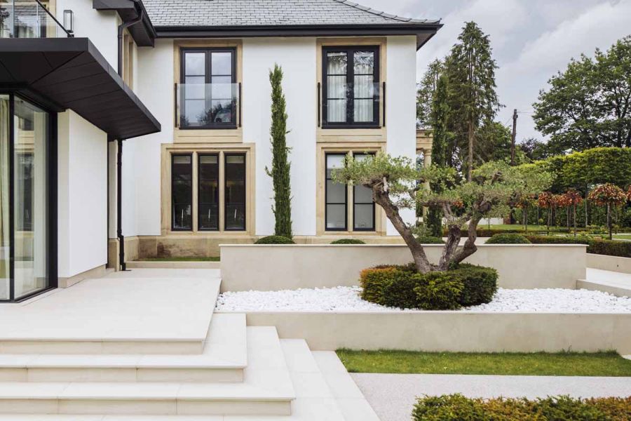 French-looking house with wrap-around patio with steps descending next to raised bed faced in Off White Premium DesignClad.