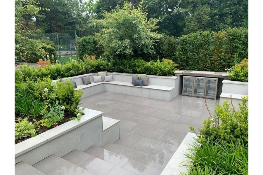Large sunken garden seating area paved in Steel Grey porcelain with built in porcelain clad benches and raised planter beds.