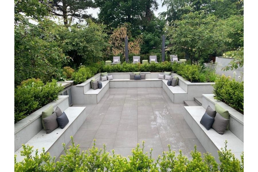 Sunken patio paved with Steel Grey porcelain, benches built in around all sides and raised planted flower beds.