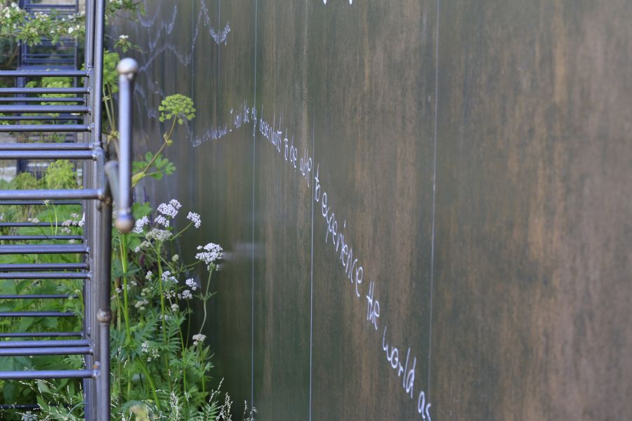 Long wall faced in large Steel Dark DesignClad external cladding panels, which have been engraved with cursive writing.