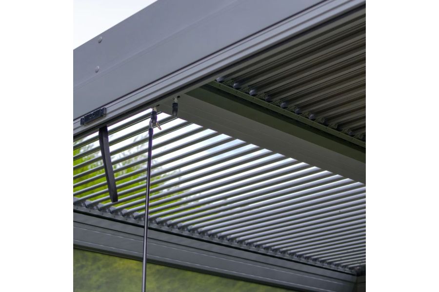 Roof of metal pergola dark grey with hand crank hooked in place, having opened one half of the louvres. Free UK delivery available.