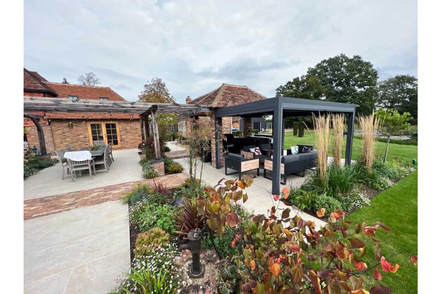 Dark Grey Metal Pergola used in large garden with other brick and wooden pergolas, paved with golden porcelain paving.