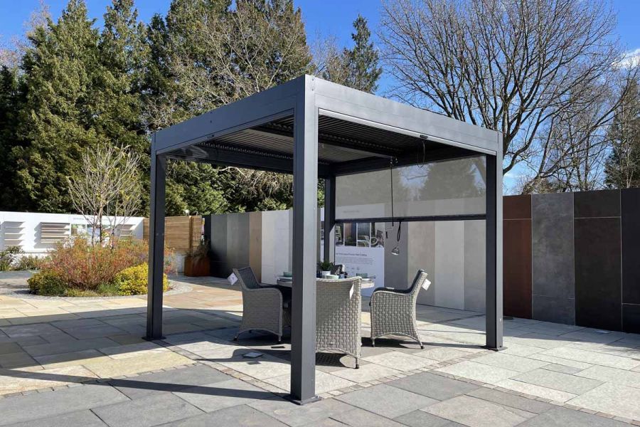 Amalfi 4-Seat garden dining set sits under Dark Grey Metal Pergola with adjustable louvres in London Stone outdoor showroom.