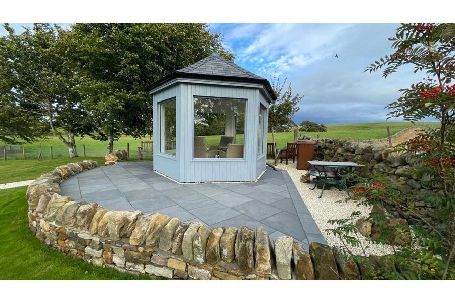 Painted hexagonal summerhouse on half-moon paved area of Midnight Black limestone and pale gravel, edged with dry stone wall.