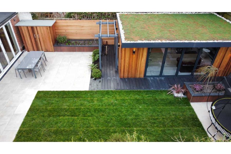 Garden office with a decking path around the outside and adjoining to a lightly coloured porcelain patio and lawn area.