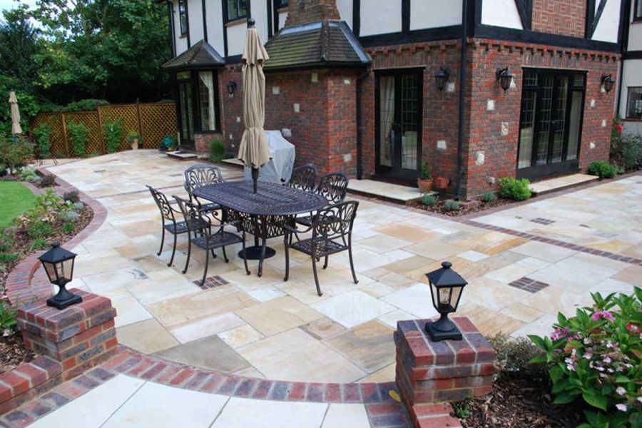6-seat metal outdoor dining set on paver-edged curved Mint Indian Sandstone patio wrapped around house. By Landscape Design Studio.
