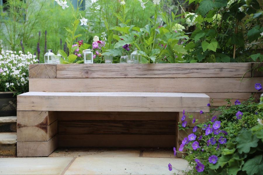 Wooden bench in front of fully planted sleeper-edged retaining bed on Mint Indian sandstone paving, with steps to left. 