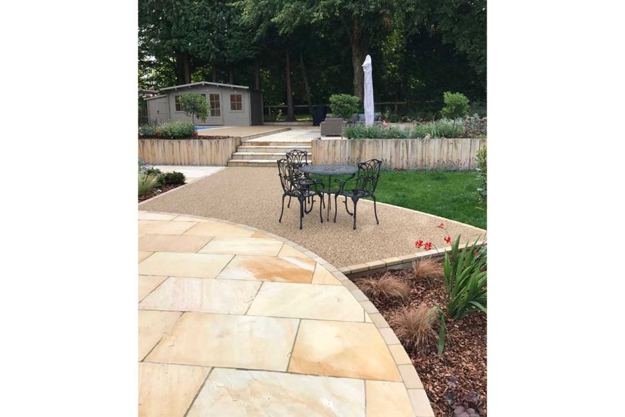 Mint Indian Sandstone, with convex edge lined with setts, next to metal dining set on bonded gravel. By Landscape Design Studio.