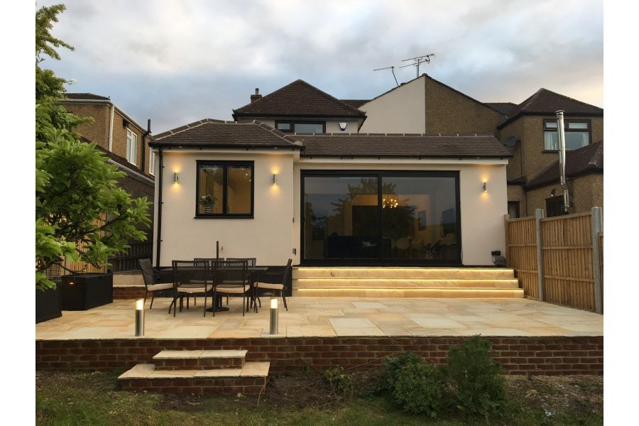 2 small steps rise from lawn to raised patio of Mint Indian sandstone paving at back of modern extension to semi-detached house.