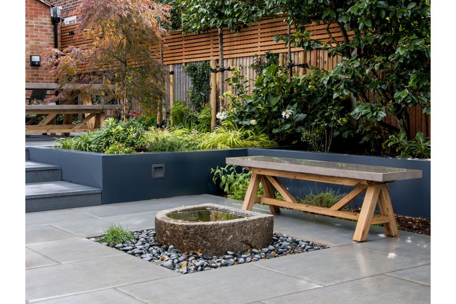D-shaped raised stone pond in square black-cobbled surround, set into Trendy Black Porcelain paving. By NLG Landscaping.