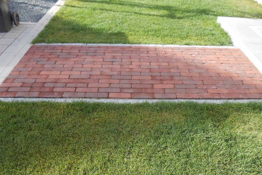 Short, wide path of red and grey Novara brick paving, part of Kessel Garden paver range, crosses grass between 2 cream paved areas.