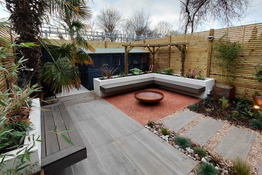 Grey wood-effect Nuage porcelain patio tiles laid with clay pavers, gravel and pebbles in garden with dry planting and shed.
