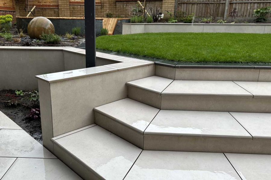 3 porcelain steps descend from lawn to paving beside flank wall faced in Off White exterior cladding. Built by CIJ Landscapes.