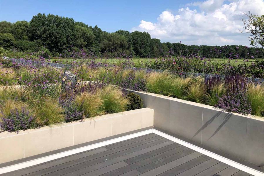Off White exterior cladding on raised beds filled with grasses and verbena, overlooking fields. By Stonecraft Landscape & Design.