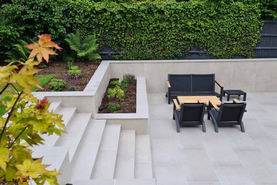 View down onto porcelain-paved seating area with luxury garden furniture, bounded by walls faced in Off White Premium DesignClad.