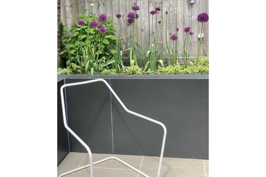 Chair outline sculpture sits in corner of paved area edged with allium-filled raised bed faced in Opium Luxury Black DesignClad.