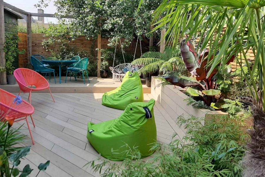 Small garden laid with Amber DesignBoard, showing deck ideas of beanbags, raised beds of sleepers, wire chairs and swing sofa.