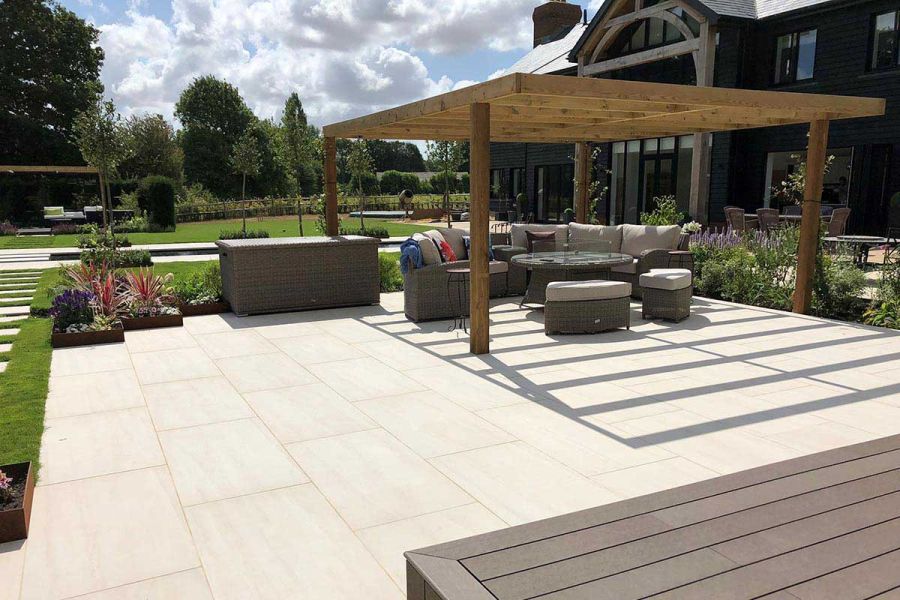 Impressive garden space paved with Faro Porcelain Paving that has luxury rattan garden furniture under a large wooden pergola.
