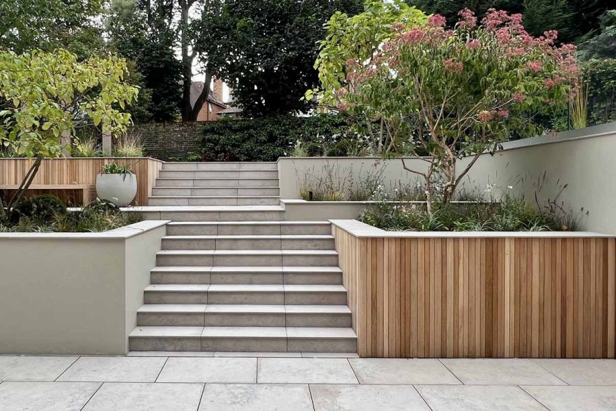 Jura Grey outdoor steps, flanked by trees in beds, rise in 2 consecutive flights from paving to upper garden level.