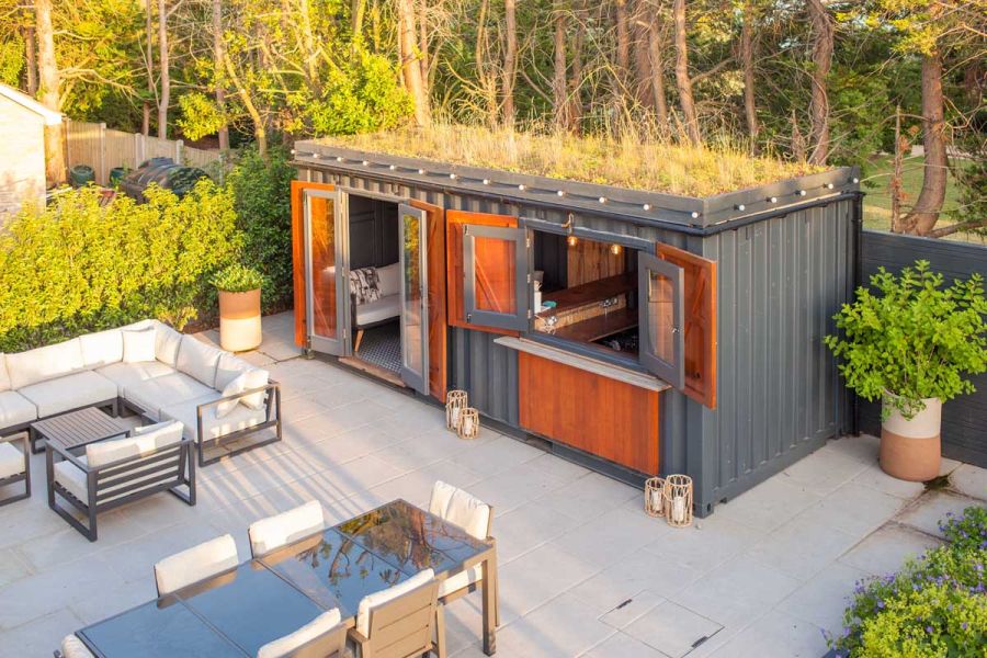 Converted shipping container sits on large area of Florence Grey porcelain paving with outdoor furniture. Design by Simon Orchard.