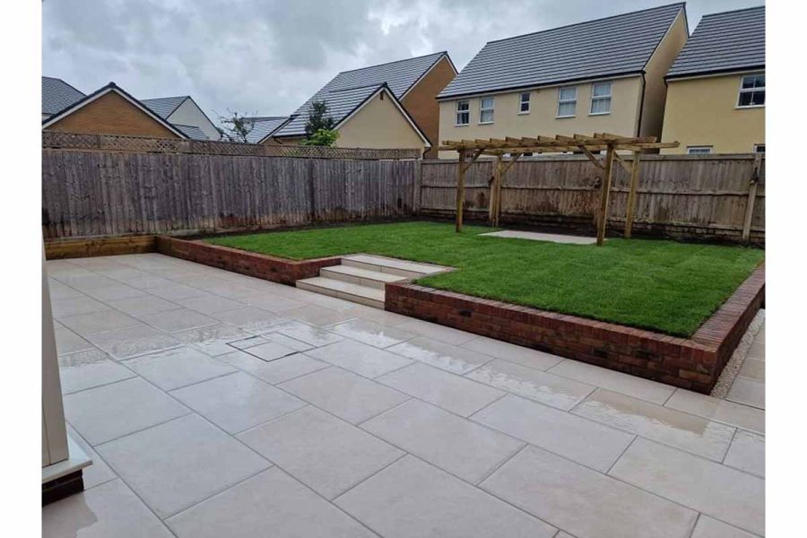 patio featuring florence white porcelain paving and steps leading up to raised lawn area with a pergola.