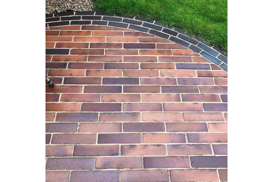 Curved edge of wet Lugano brick paving, set into lawn, provides border to Bromley clay pavers laid in running bone pattern.