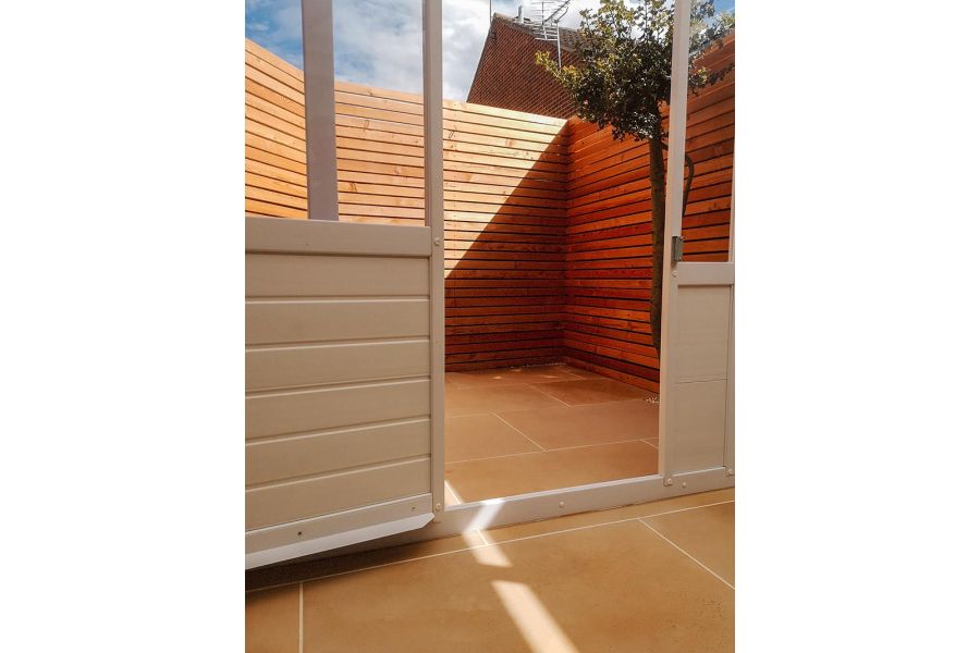 View through open sliding door to tiny area paved in Dune smooth sandstone paving with high slatted fence. Design by Vu Garden.