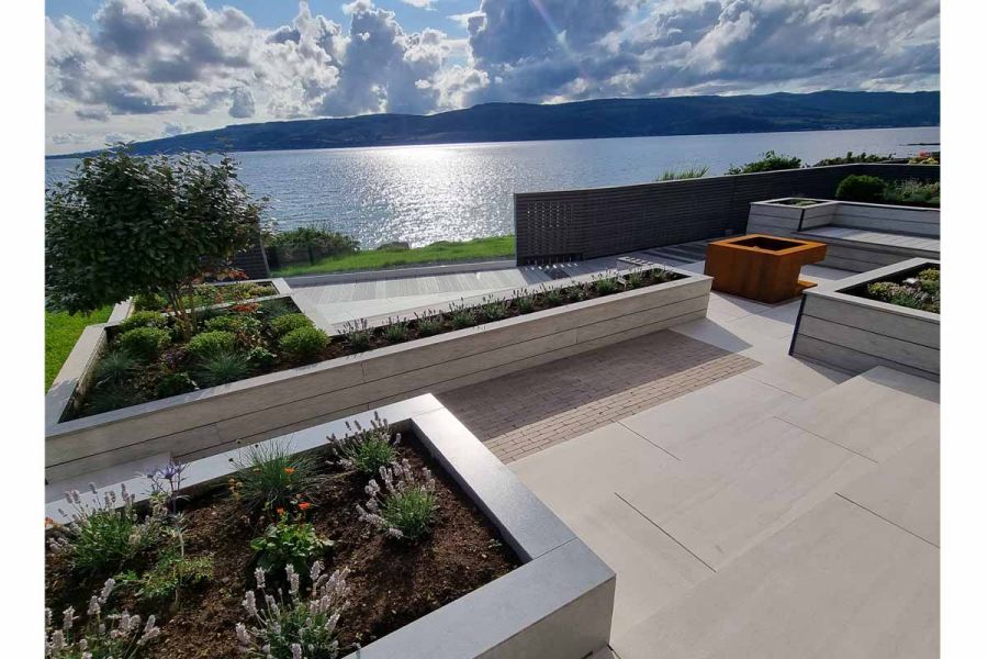 3 steps descend to area paved with Faro porcelain outdoor tiles and clay pavers, overlooking view water and distant hills.