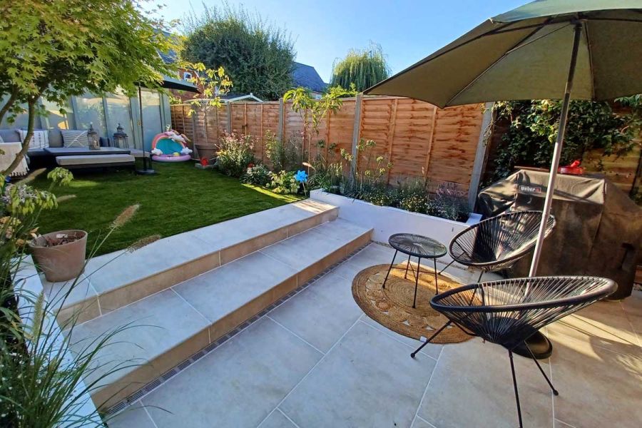 Small back garden with Cream porcelain patio and steps leading up to a raised artificial lawn and comfortable seating area.