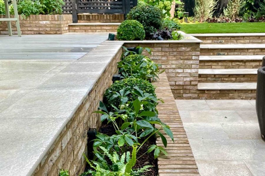 Gea porcelain 20mm bullnose steps with brick risers ascend to lawn and patio area with matching paving by Hampstead Garden Design.
