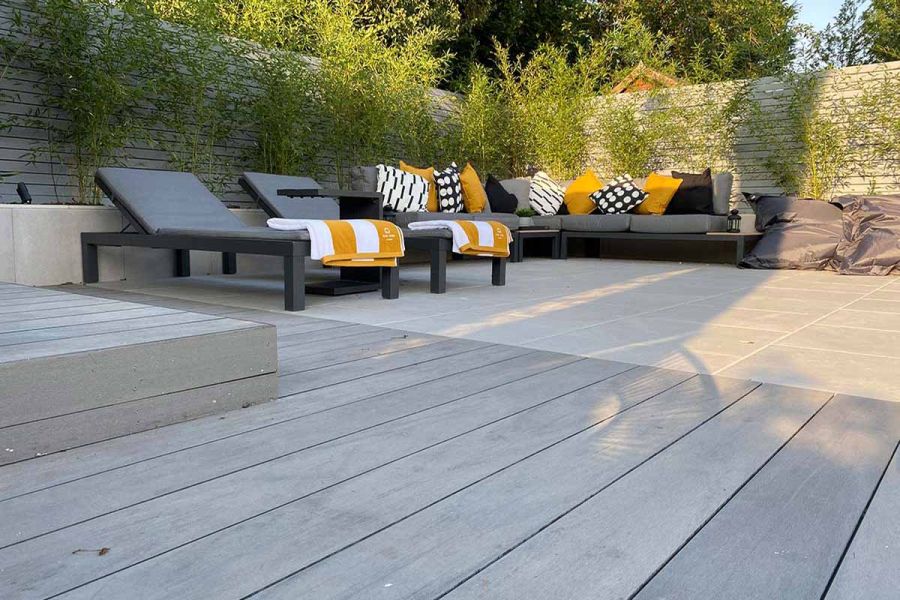 Pebble Grey Brushed composite deck with matching step by Limebok Landscaping. Sunloungers and corner sofa on paved area beyond.