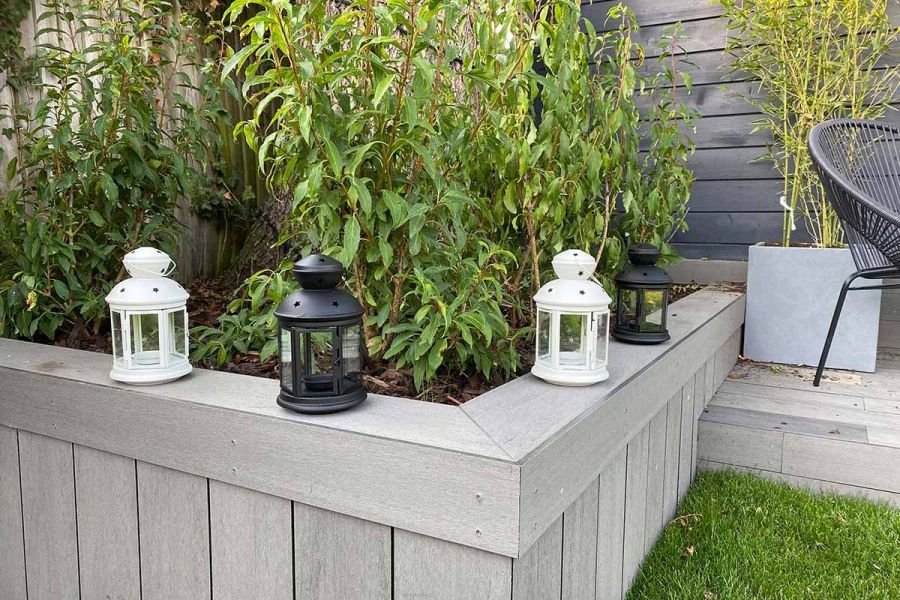 White and grey lanterns sit on edge of raised bed filled with tall shrubs and faced with Pebble grey brushed composite decking.
