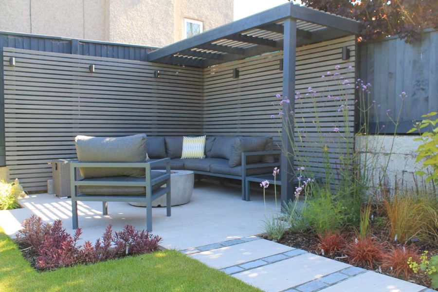 Paved seating area in garden corner, partially covered by pergola, with a tall garden screen of Pebble Grey battens on 2 sides.