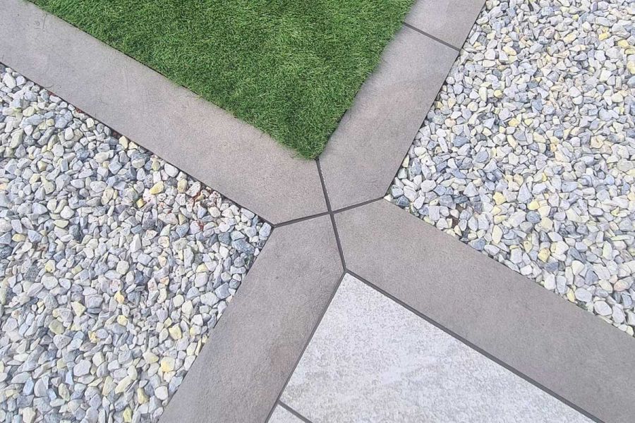 4 Steel Grey porcelain planks with mitred ends form a cross, edging gravel, grass and paving squares. By Aspen Landscape Design.