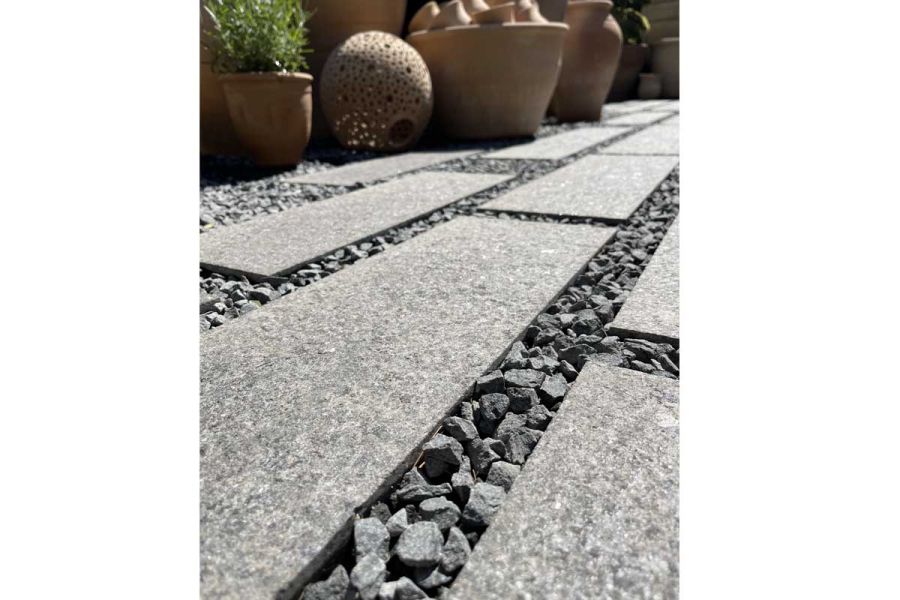 Ground-level view of Dark Grey Granite Plank Paving, slabs separated by gravel. Pots in background. Design by The Outdoor Room.