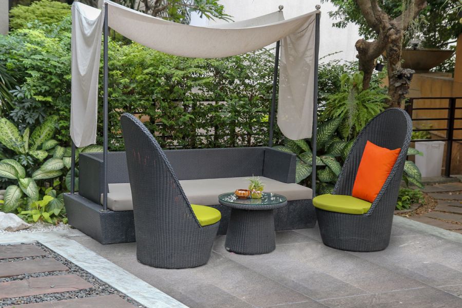 Tall wicker garden chairs and sofa covered by a shade sail and sitting on top of a Platinum Grey porcelain patio.