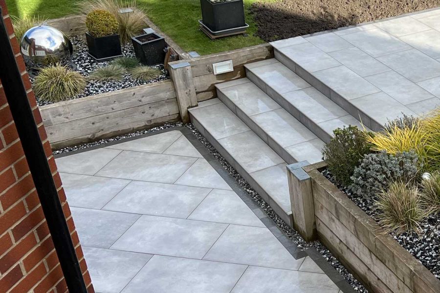 4 steps descend between wooden raised beds to paved area edged with Platinum Grey small porcelain patio tiles.