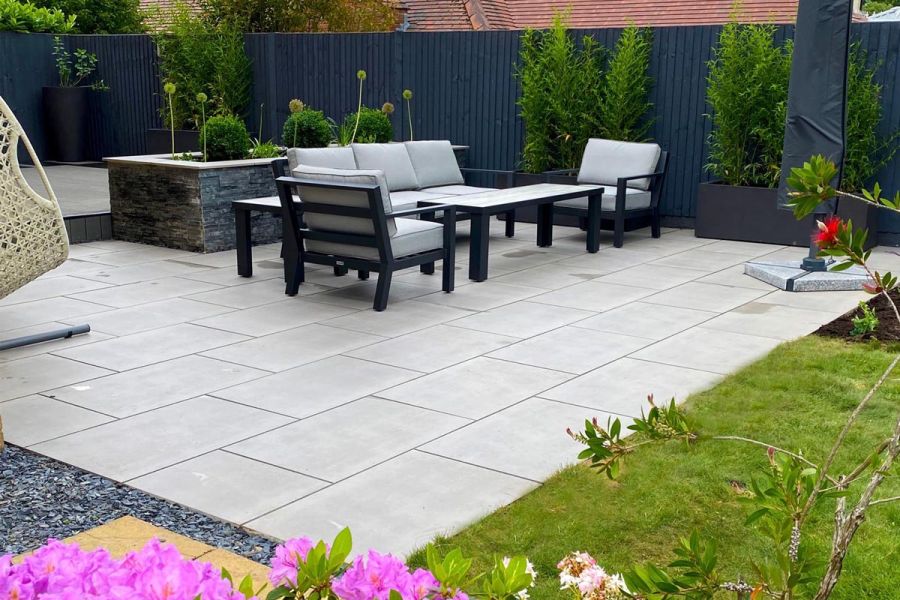 Looking across a back garden porcelain patio and outside dining area with stone clad raised beds and fibreglass planters.