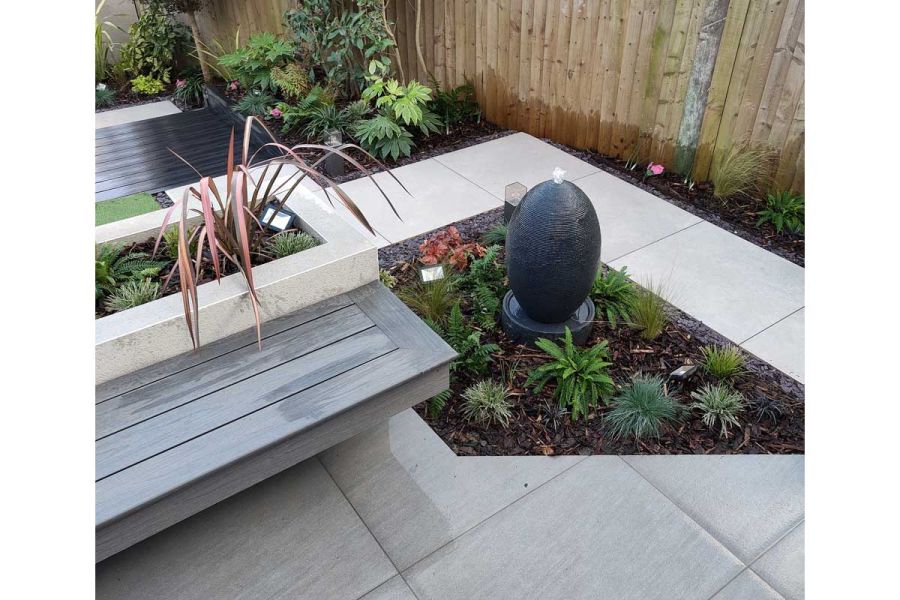 Right-angled trapezium-shaped bed with fountain set in Polvere 800x800 porcelain paving, next to raised bed with plank-top bench