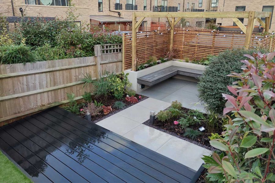 Polvere Porcelain Large Paving Slabs laid with decking and grey tiles, in fenced back garden seating area, with rectangular beds.