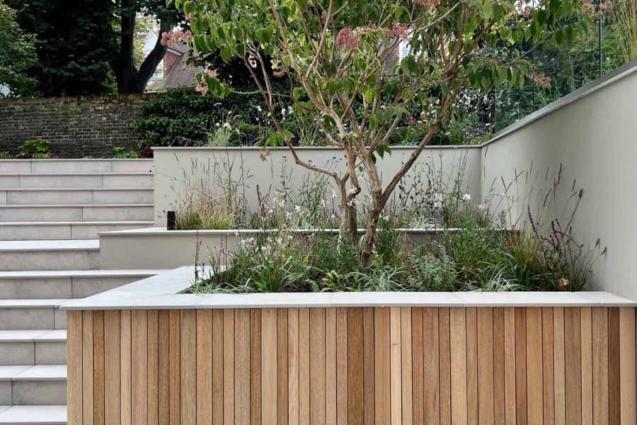 Jura Grey porcelain smooth coping stones top wood-clad raised beds in terraced garden with lots of matching steps.