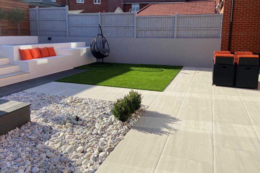 Low maintenance back garden paved in Faro porcelain with gravel and artificial grass section and an egg chair.