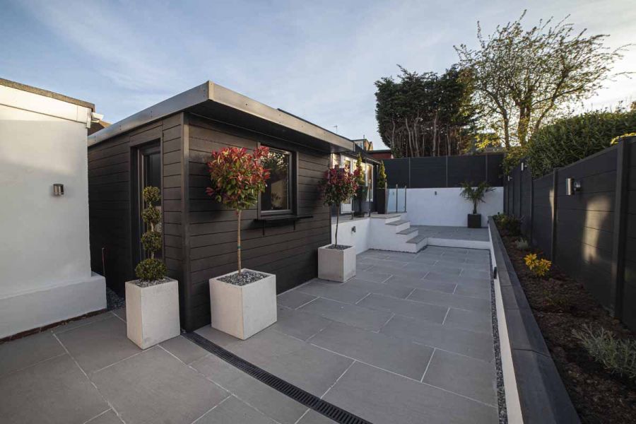 2 garden rooms with planters on left of long garden wholly paved in Urban Grey porcelain, raised bed and fence on right.