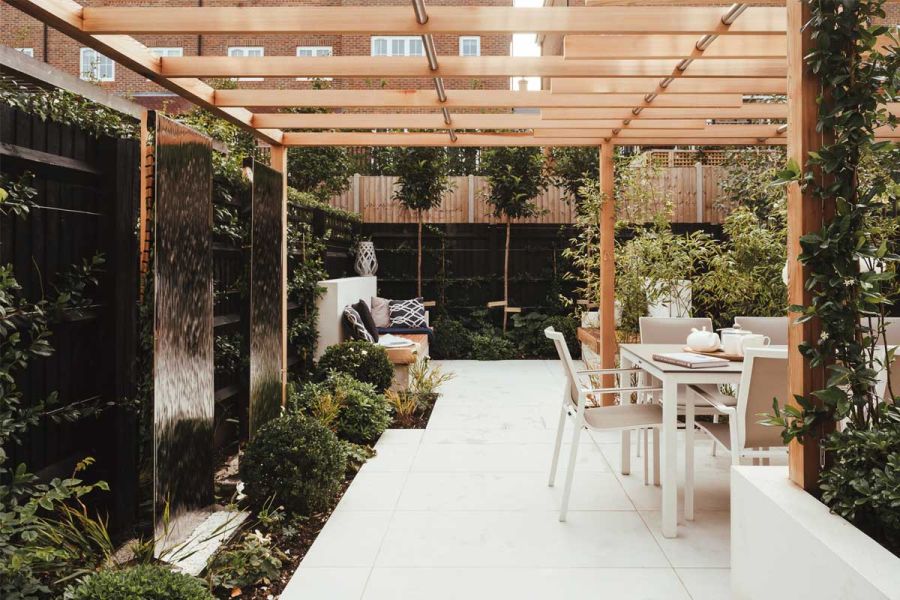 Comblanchien Porcelain Paving beneath wooden pergola, with stainless steel water wall, clipped planting and outdoor dining set.